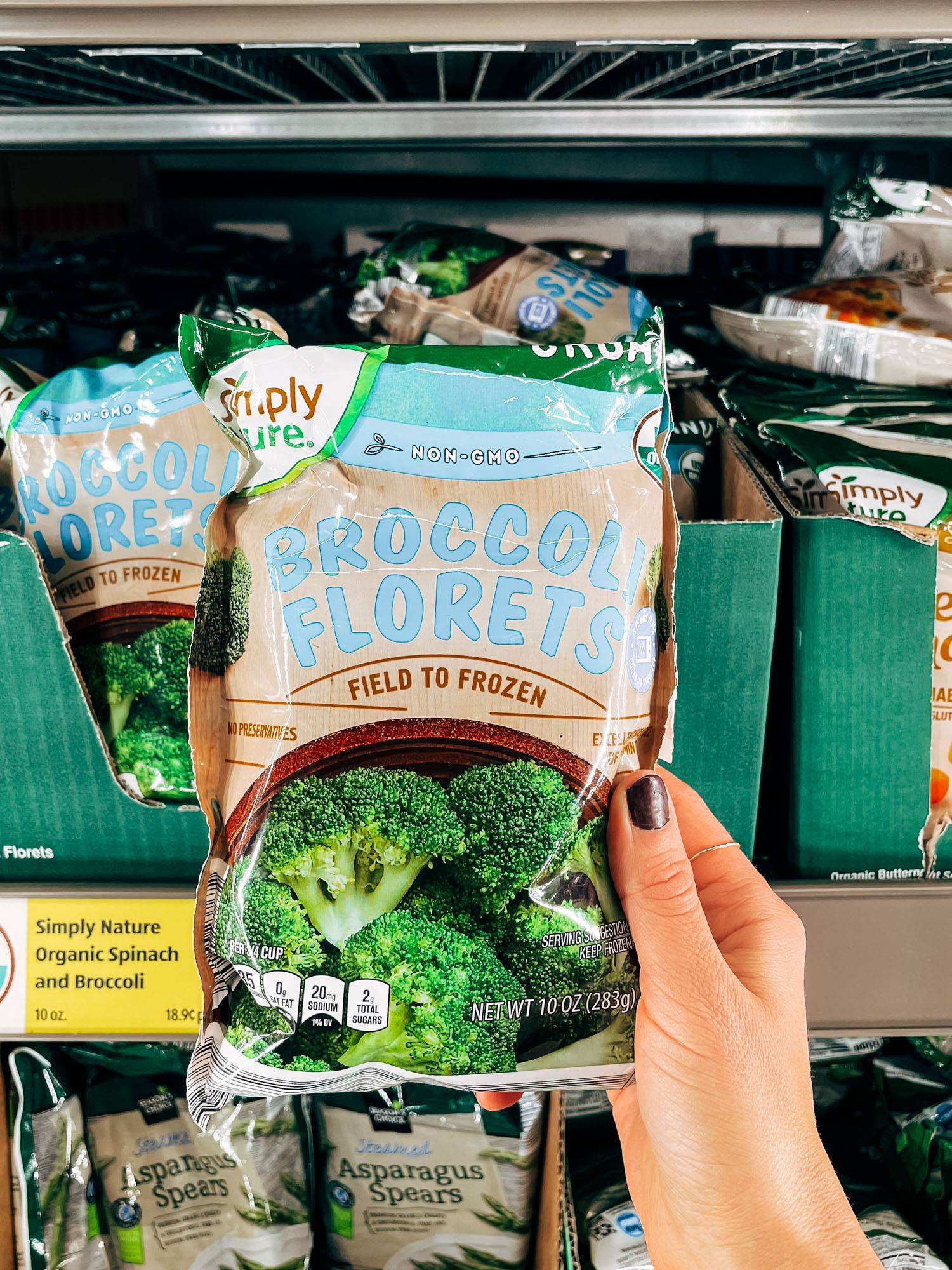 White hand holding a bag of frozen broccoli