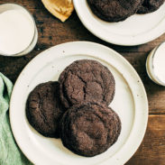 Dark chocolate cookies on a plate next to a glass of milk.