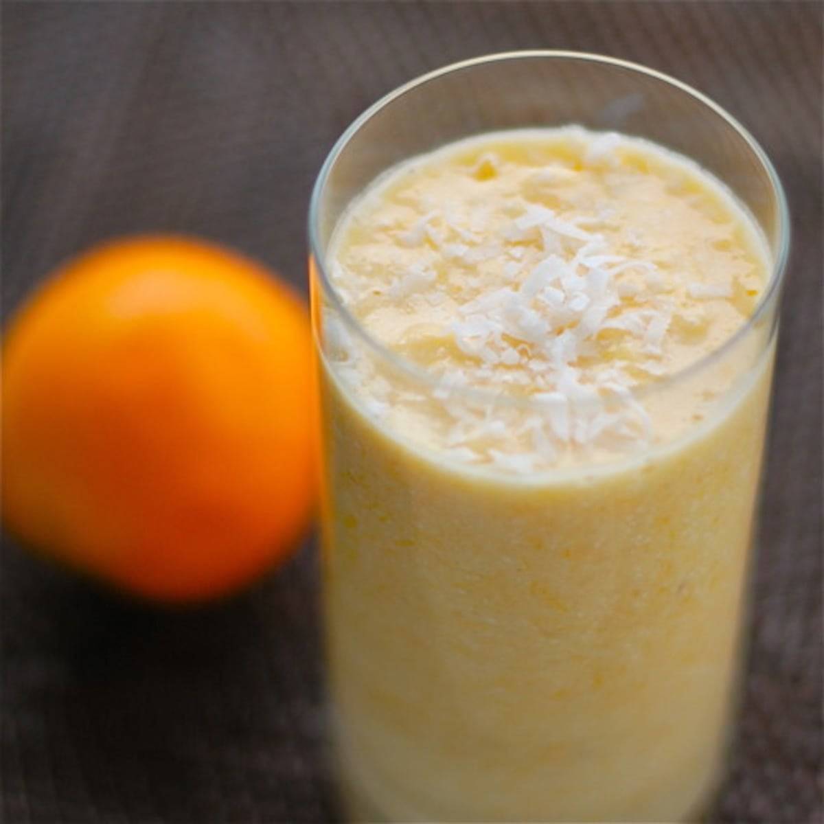 Coconut pineapple orange smoothie in a glass next to an orange.