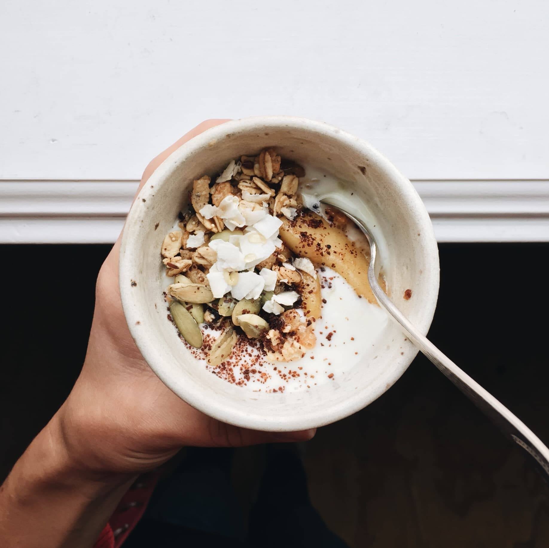 hand holding a bowl of food with coconut flakes